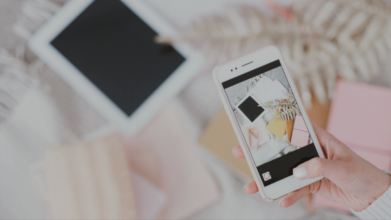 smartfon w białej obudowie w dłoni, robi zdjęcie tabletowi leżącemu na łóżku na jasnej narzucie
